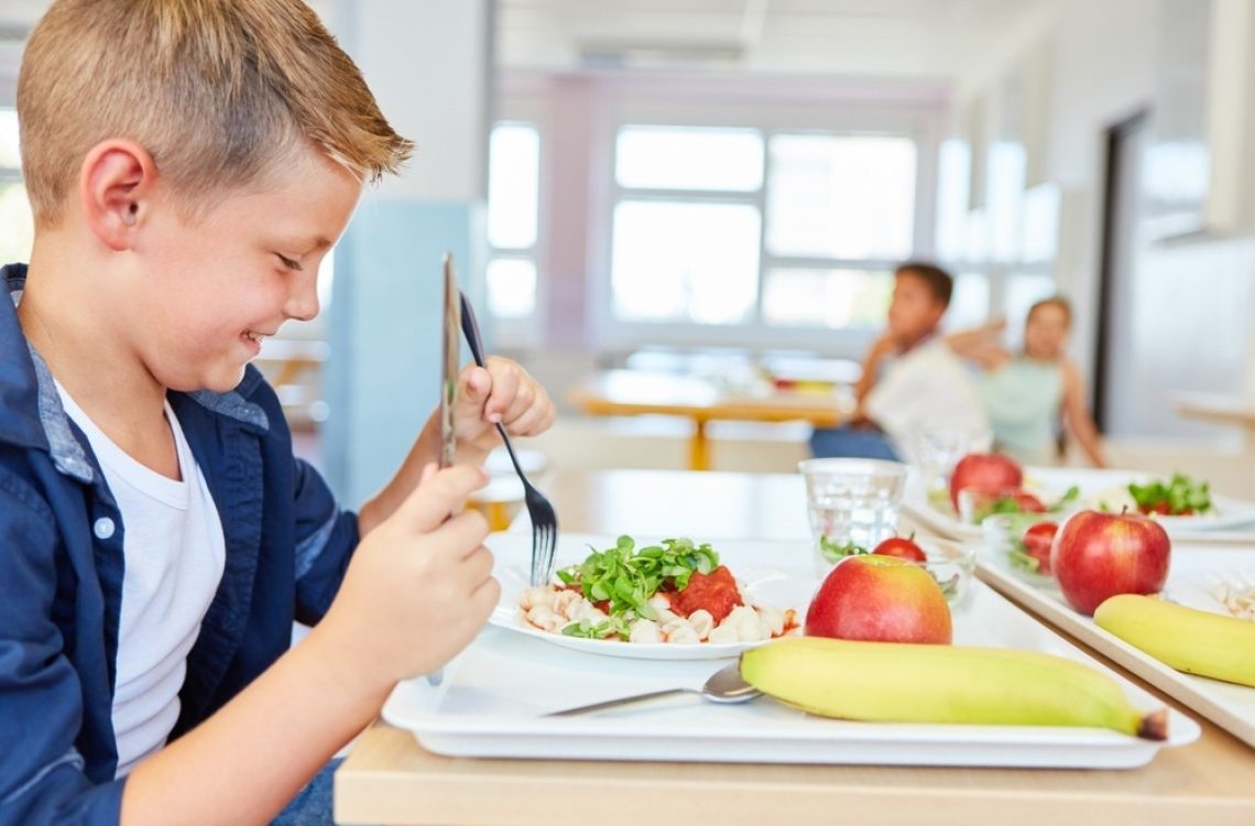 Happy,Schoolboy,Eating,Meal,With,Cutlery,While,Sitting,At,Table